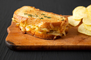 Homemade French Onion Melt Cheese Sandwich with Chips on a rustic wooden board on a black surface, side view. Close-up.