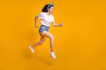 Fototapeta na wymiar Full length body size photo of cheerful young woman running fast jumping high hurrying up on sale isolated on bright yellow color background