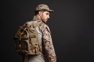 Confident masculine military man in uniform posing with backpack