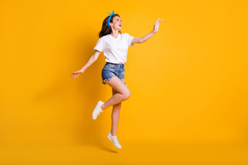 Fototapeta na wymiar Full length body size photo of careless girl jumping up touching empty space with hand on vivid yellow color background