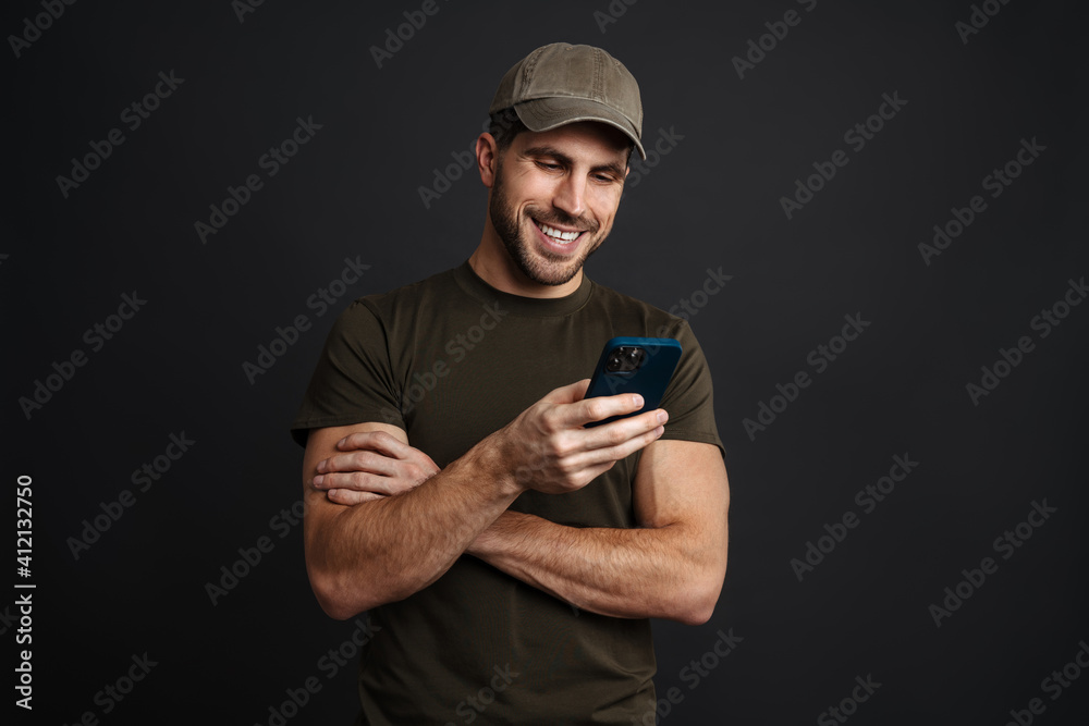 Wall mural Happy masculine military man smiling and using mobile phone