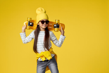 cute little child girl in hat and sunglasses posing with yellow skateboard on studio background. copy space © Rychko Yevhen