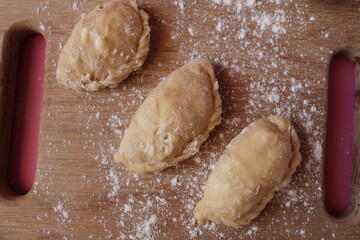 Raw cooking dumplings lie on a board beside egg flour on a pink background view from above