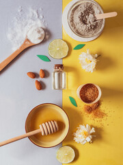 natural skin care products: backing soda, clay powder, honey, brown sugar, almond oil. Colorful background of natural cosmetics and flowers.  body scrubs on grey and yellow back