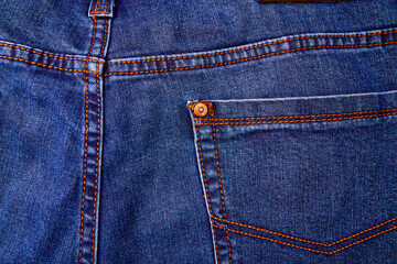 Fototapeta premium Blue denim jeans background pocket with seam and orange thread stitches.