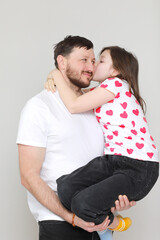 young dad holds his little daughter in his hands. father hugging his child with love and child kiss him. man in white t-shirt and girl in t-shirt with red hearts. Happy Father's Day. valentine's day