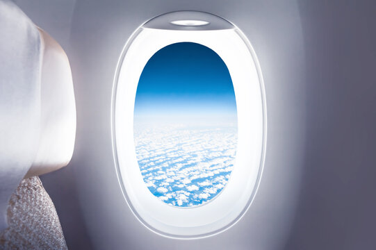 Airplane window with a view of blue sky with clouds. Travel and vacation concept background