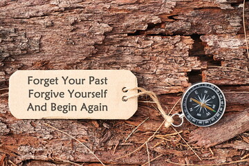 Conceptual Image: Magnetic compass with paper tag written Forget Your Past, Forgive Yourself And Begin Again, selective focus.