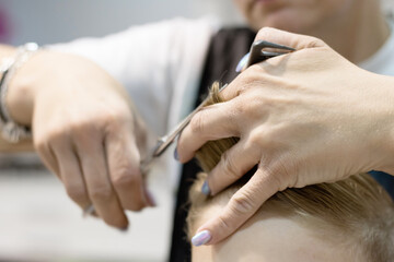 Obraz na płótnie Canvas Close-up of female hairdresser cutting boy's hair at the salon.