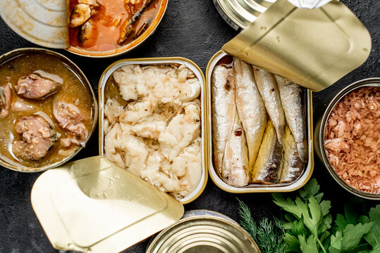 Assortment of canned food cans with different types of fish Salmon, tuna, mackerel and sprats and seafood on a stone background with copy space for your text