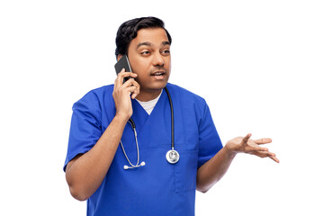 healthcare, profession and medicine concept - indian doctor or male nurse in blue uniform with stethoscope calling on smartphone over white background
