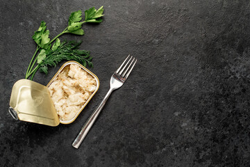 Tinned sprats in a tin can with a fork on a stone background with copy space for your text