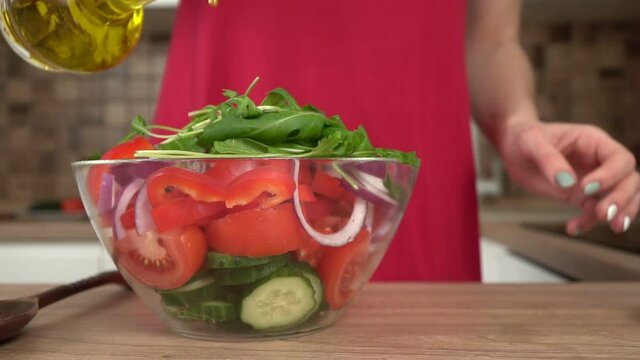 A woman in the kitchen pours a vegetable salad with olive or sunflower oil