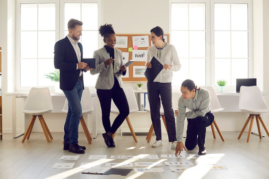 Enjoying Teamwork. Happy Young Diverse People Analyzing Sales Growth Data Reports With Charts And Graphs In Modern Office. Team Of International Employees Developing Business Strategy In Group Meeting