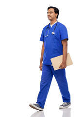 healthcare, profession and medicine concept - happy smiling indian doctor or male nurse in blue uniform with clipboard and stethoscope walking over white background