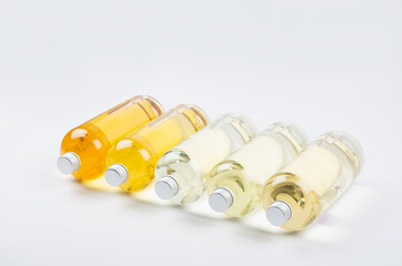 Collection transparent lying bottles with different pale colors liquid, cosmetic product, perfume or drink and silver cap in diadonal row on white background, side view.