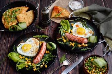 Homemade breakfast concept. Appetizing scrambled eggs, sausages, vegetables and herbs on dark plates on a rustic background.