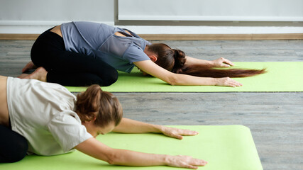 Fototapeta premium Two women playing yoga, stretching body on the floor together
