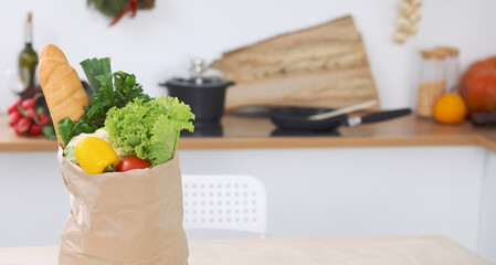 Paper bag full of vegetables on the table in kitchen interiors. Healthy meal and vegetarian concept