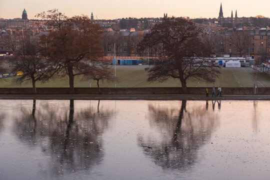 Frozen Winter Pond At Inverleith Park In The Stockbridge Neighbourhood With Edinburgh City Skyline In The Background At Sunset Or Sunrise.