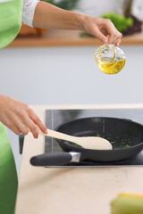 Young woman housewife cooking in the kitchen while adding olive oil. Concept of fresh and healthy meal at home