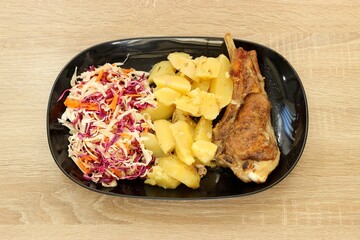 Baked potatoes, roasted pork chop and cabbage salad in a plate isolated on a wooden table. Top view, selective focus