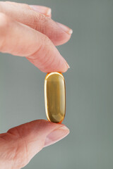 Female hand holding a big yellow capsule of nutritional supplement . Food supplement, vitamin D,...