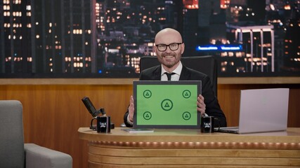 Late-night talk show host showing a green board with tracking points to audience in a studio. TV...