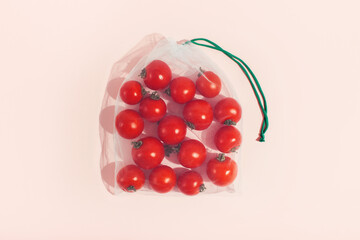 Reusable packaging of products by weight. Red tomatoes in a reusable bag close up on a pink background.