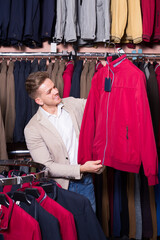 Fototapeta na wymiar Happy male customer examining coats in men cloths store