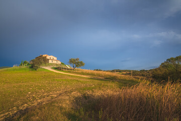 A lone rural countryside farmhouse in Radicondoli catches some golden sunset or sunrise light with a moody dark blue sky as a backdrop in Tuscany, Italy.