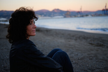 Adult woman sitting on the beach looking at the sea during sunset