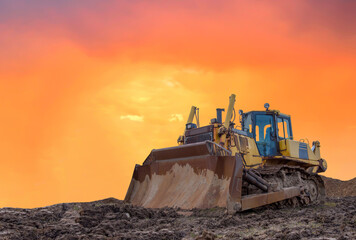 Dozer on earthmoving at construction site on sunset background. Construction machinery and...