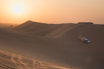 Obraz na płótnie Canvas A 4x4 sport utility vehicle bashing sand dunes at sunset on a tourist desert safari in the Empty Quarter Desert (Rub' al Khali) near Abu Dhabi, UAE.