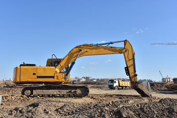Fototapeta na wymiar Excavator on earthworks at construction site. Backhoe on foundation work and road construction. Heavy machinery and construction equipment