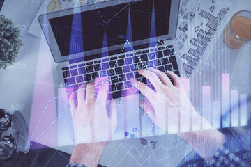 Double exposure of man's hands typing over laptop keyboard and forex chart hologram drawing. Top view. Financial markets concept.