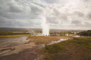 Strokkur Geysir hot spring erupts to an audience of tourist spectators in the Haukadalur Valley of Southwestern Iceland.