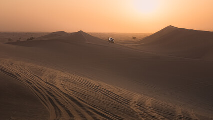 Fototapeta na wymiar A 4x4 sport utility vehicle bashing sand dunes at sunset on a tourist desert safari in the Empty Quarter Desert (Rub' al Khali) near Abu Dhabi, UAE.