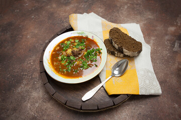 Homemade thick soup kharcho with beef and tomato paste is poured into a plate, next to it there is black bread. Served table.