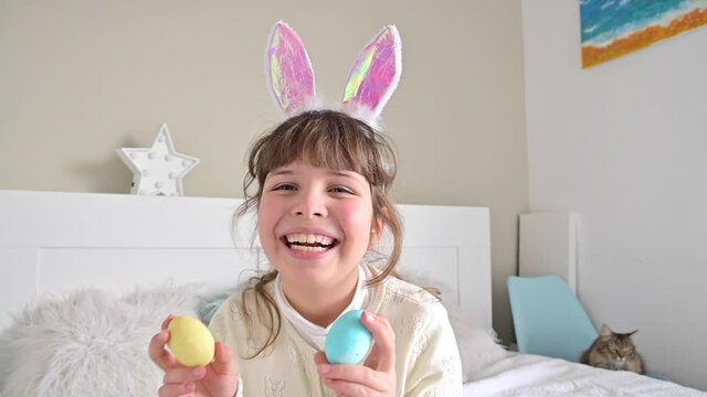 Little girl with bunny ears is having fun and playing with Easter eggs of different colors. Fun at Easter.