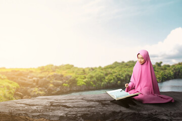 Asian Muslim woman in a veil sitting and reading the Quran