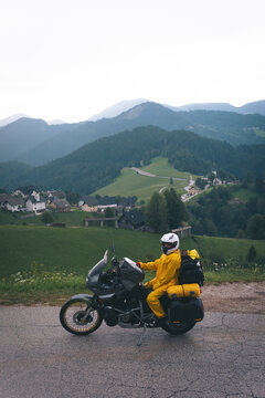 A girl in a yellow raincoat, shoe covers and a motorbike helmet. Motorcyclism and travel. Vertical photo. Top of the Mountains. A day with clouds. Difficult test and extreme vacation. Biker outfit.