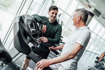 Portrait of a young trainer in the gym, it includes a treadmill for an older man