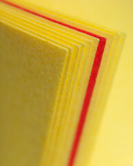 One sheet of orange paper between several yellow ones, closeup 1