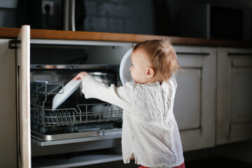 Fototapeta na wymiar child toddler unloads the dishwasher on his own in a Scandinavian-style kitchen, child's mother's helper, housework with the child, household chores, household