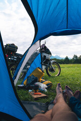 Vertical view from camp tent door. Motorcycle adventure bike on the background of green grass,...