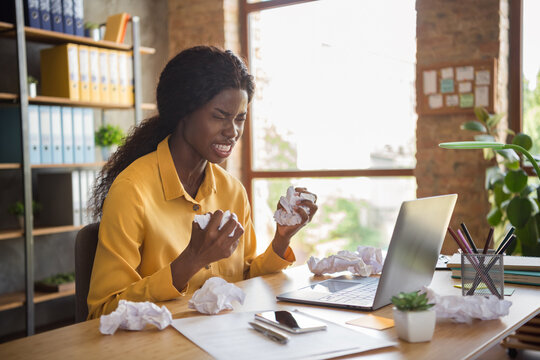 Photo of furious dark skin business woman hold crumple hands paper sit desk in office indoors workstation