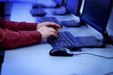 The man's hands work on a black keyboard on a personal computer. Esports player. Dark lighting in the office.