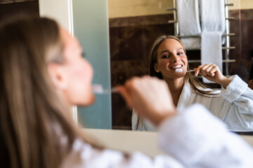 Portrait of young woman with a smile brushing her teeth in bathroom