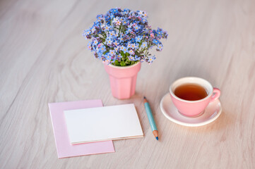 A bouquet of forget-me-not flowers on a table with a cup of tea and card for congratulation text. Holiday background, copy space, soft focus. Mothers day, birthday concept.